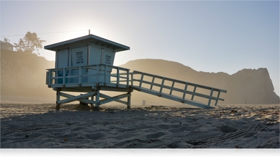 photo of a lifeguard stand on the beach with the sun backlighting it