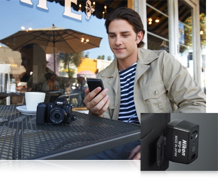 photo of a man at an outdoor cafe holding a smartphone and a close up shot of the WU-1b device in the Nikon 1 V2