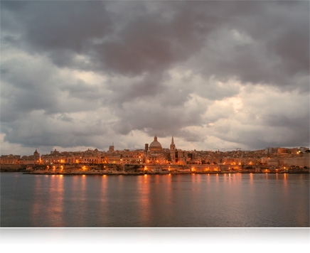landscape photo of a waterfront city with clouds, in low light with city lights on