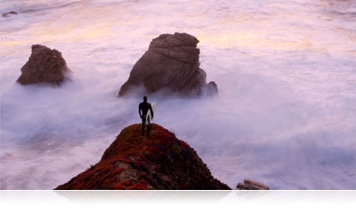 Photo of a surfer standing on a rock overlooking the water