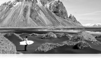 Black and White photo of a surfer at a rocky shoreline with his surfboard